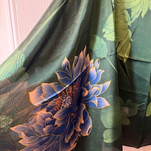 May include: Dark green fabric with a large blue and orange floral design. The fabric has a semi-transparent quality, with a detailed illustration of a lotus flower. The background features green leaves and a darker green hue.