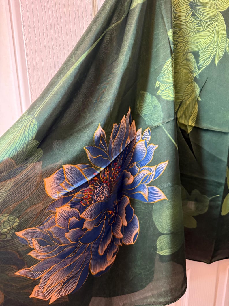 May include: Dark green fabric with a large blue and orange floral design. The fabric has a semi-transparent quality, with a detailed illustration of a lotus flower. The background features green leaves and a darker green hue.