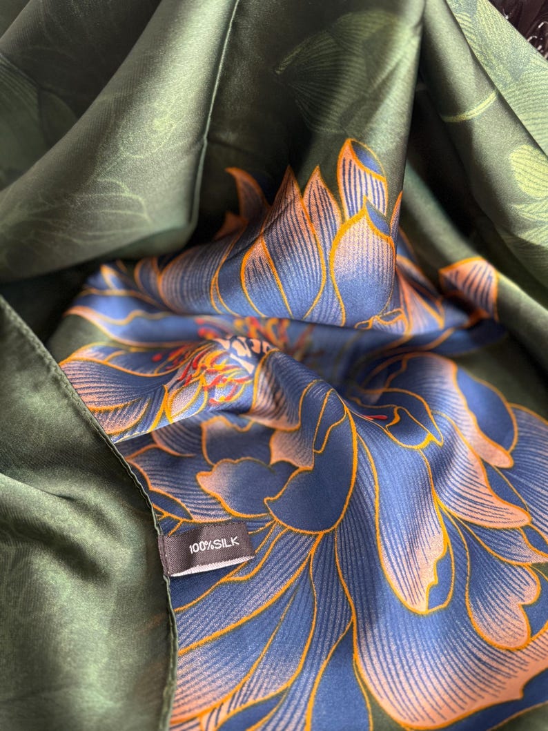 May include: A dark green silk scarf with a floral pattern in shades of blue and orange. The scarf is folded, revealing the intricate design. A small tag reads "100% SILK".