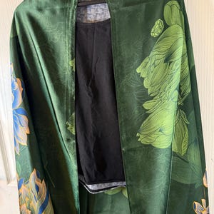 May include: A dark green kimono-style wrap with a floral pattern in shades of green, blue, and gold. The wrap is draped over a black top. The brand "EA7" is visible on the collar.