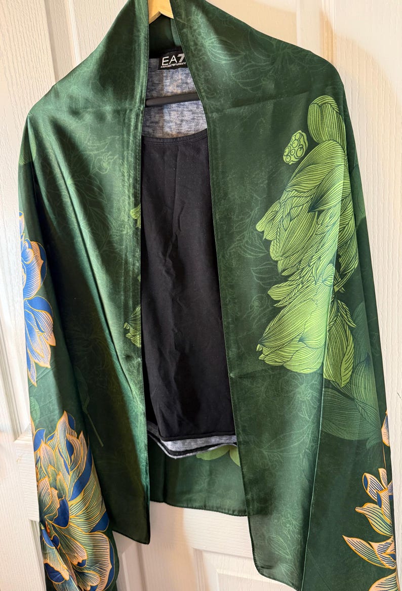 May include: A dark green kimono-style wrap with a floral pattern in shades of green, blue, and gold. The wrap is draped over a black top. The brand "EA7" is visible on the collar.