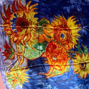 May include: A scarf featuring a vibrant painting of sunflowers in shades of yellow, orange, and red against a deep blue background. The artwork is reminiscent of Van Gogh's style, with visible brushstrokes and a textured appearance.