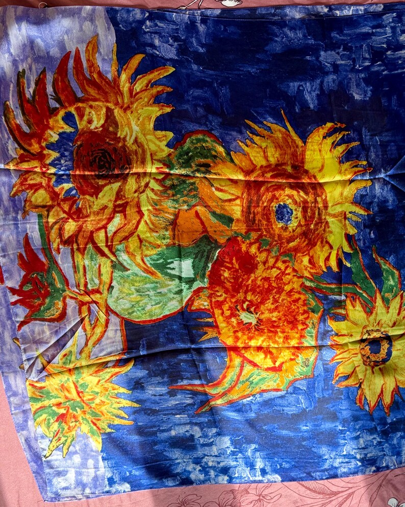 May include: A scarf featuring a vibrant painting of sunflowers in shades of yellow, orange, and red against a deep blue background. The artwork is reminiscent of Van Gogh's style, with visible brushstrokes and a textured appearance.
