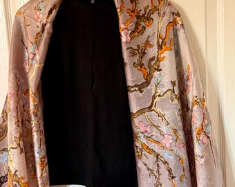 May include: A black top with a floral patterned scarf draped over it. The scarf features a light purple background with branches, orange, pink, and blue flowers. The top is hanging on a wooden hanger.