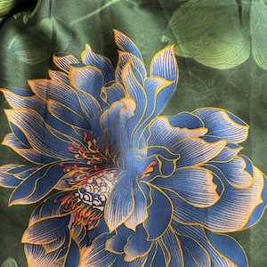 May include: A dark green silk scarf featuring a large blue and gold floral design. The flower has intricate details with a mix of blue, gold, and red accents. The background has green leaves.