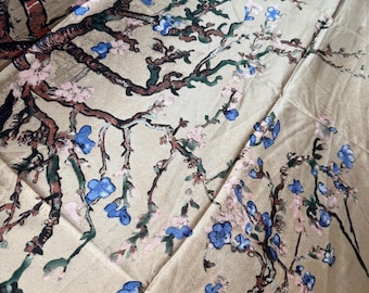 May include: A beige fabric with a floral design featuring branches with blue and pink flowers. The branches are brown and green, creating a natural and artistic pattern. The fabric has a soft, flowing appearance.