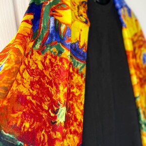 May include: A vibrant, colorful kimono-style garment with a floral design in shades of yellow, red, blue, and green. The kimono is draped over a black top, creating a striking contrast. The garment is hanging on a wooden hanger.