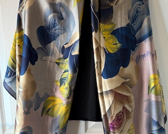 May include: A silky scarf with a floral rose pattern in shades of blue, yellow, and cream. The scarf is draped over a black garment, showcasing the intricate design and color palette. The scarf has a dark blue border.
