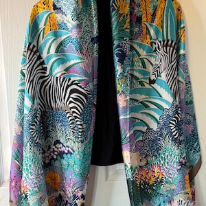 Può includere: Una sciarpa colorata con stampa giungla e zebra. La sciarpa presenta un design vibrante con sfumature di blu, verde, giallo e viola. La stampa zebrata aggiunge un tocco unico al design generale.