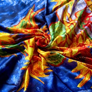 May include: A vibrant, colorful fabric featuring a repeating pattern of sunflowers against a blue background. The sunflowers are depicted in shades of yellow, orange, red, and green, with a textured, painterly style. The fabric is likely silk or a similar material.