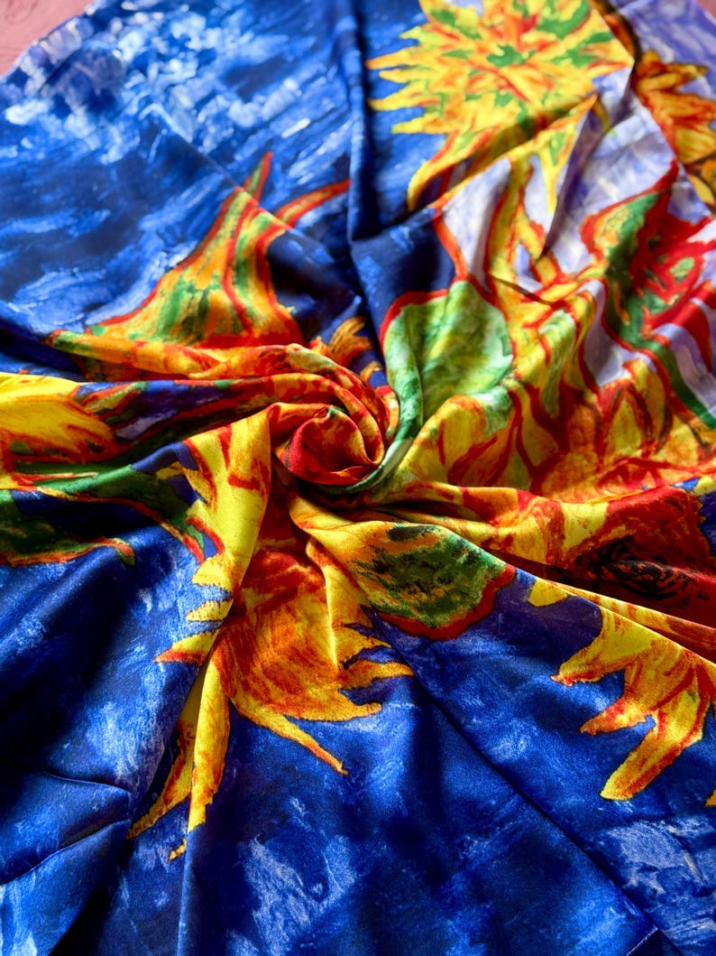 May include: A vibrant, colorful fabric featuring a repeating pattern of sunflowers against a blue background. The sunflowers are depicted in shades of yellow, orange, red, and green, with a textured, painterly style. The fabric is likely silk or a similar material.