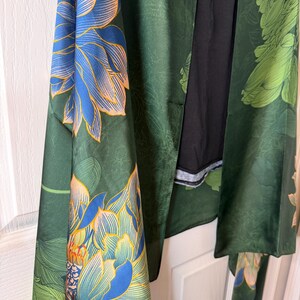 May include: A dark green kimono-style robe with large floral patterns in blue and peach. The robe has long sleeves and a black interior. The floral design is repeated throughout the garment, creating a cohesive and artistic look.