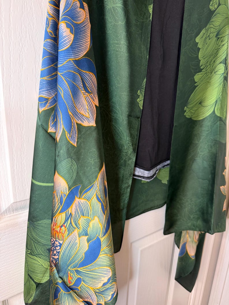 May include: A dark green kimono-style robe with large floral patterns in blue and peach. The robe has long sleeves and a black interior. The floral design is repeated throughout the garment, creating a cohesive and artistic look.