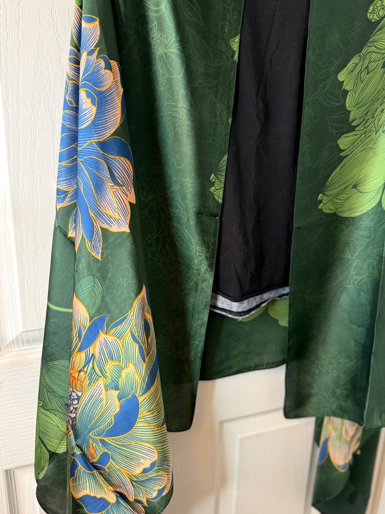 May include: A green floral kimono with blue and peach-colored flower designs. The kimono is made of a silky material and has long sleeves. The background is a white door.
