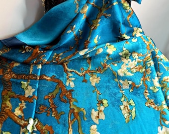 May include: A vibrant blue silk scarf featuring a floral design reminiscent of Van Gogh's Almond Blossoms. The scarf is draped over a brown leather handbag, showcasing the intricate details of the artwork. The scarf's color palette includes shades of blue, brown, and white.