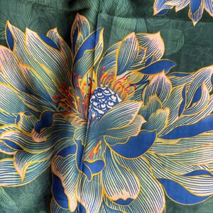 May include: A dark green textile with a large, detailed floral pattern. The flower features blue and yellow petals with intricate line details, and a central design with red and blue accents. The background has a subtle leaf pattern.