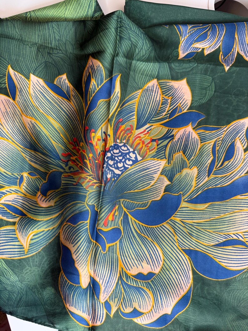 May include: A dark green textile with a large, detailed floral pattern. The flower features blue and yellow petals with intricate line details, and a central design with red and blue accents. The background has a subtle leaf pattern.