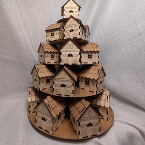 May include: A wooden advent calendar in the shape of a tiered village. Each small house is numbered and features a detailed roof, door, and windows. The houses are arranged on circular platforms, creating a festive display.
