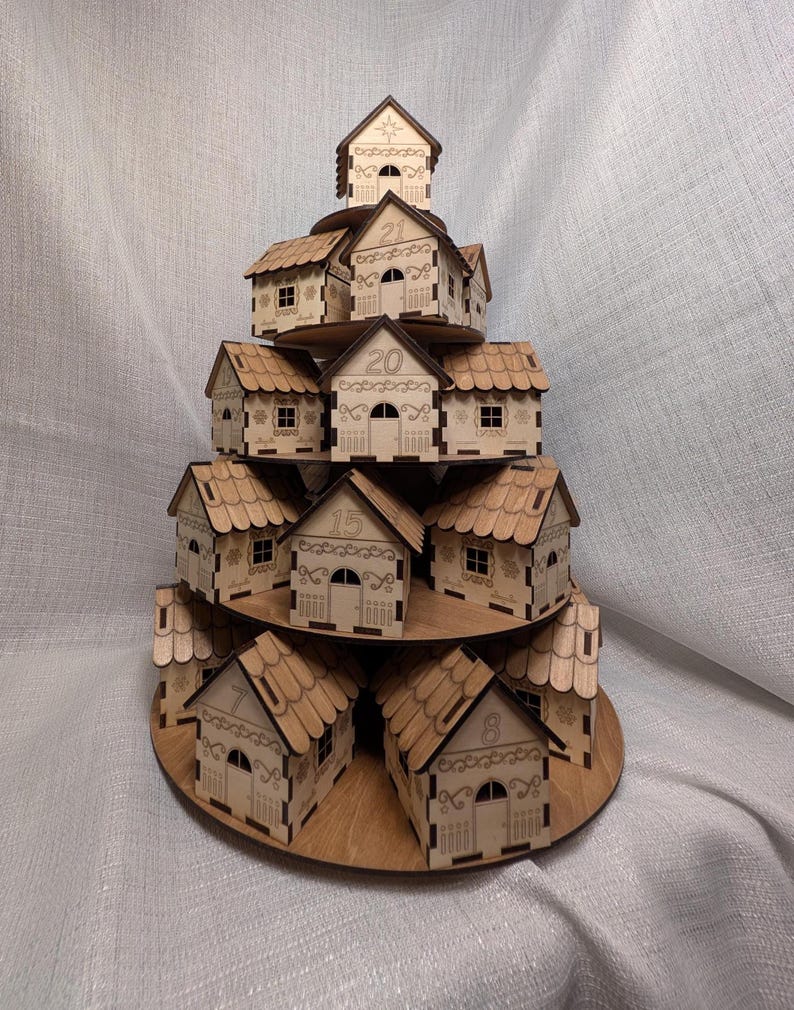 May include: A wooden advent calendar in the shape of a tiered village. Each small house is numbered and features a detailed roof, door, and windows. The houses are arranged on circular platforms, creating a festive display.
