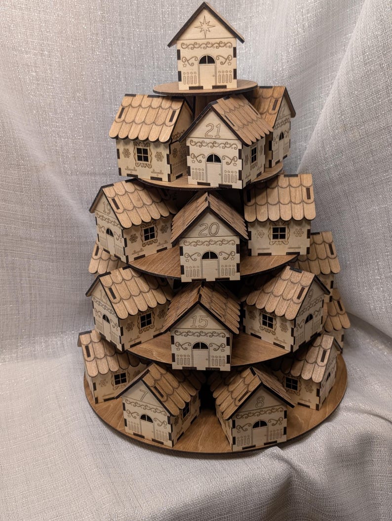 May include: A tiered wooden advent calendar in the shape of a Christmas tree. The natural wood houses are numbered and feature decorative cutouts. The houses are arranged on circular platforms, creating a festive display.