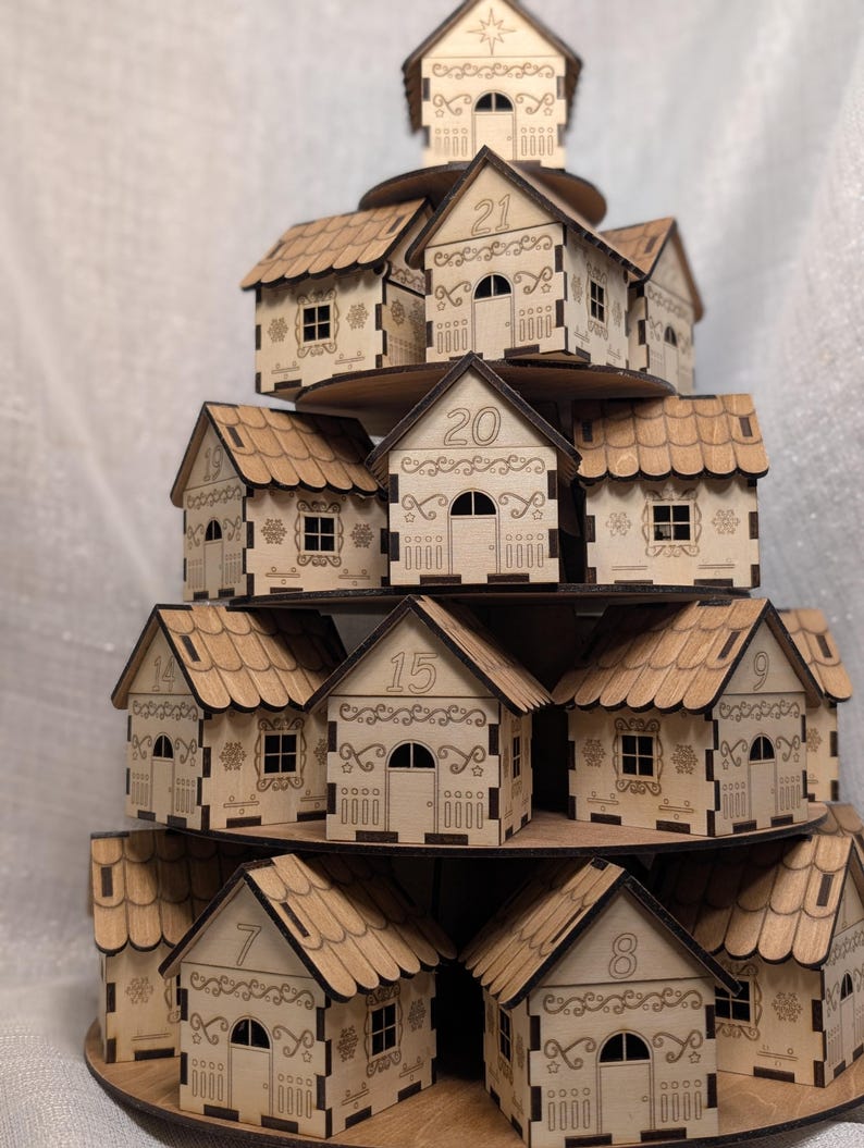 May include: A tiered wooden advent calendar in the shape of a Christmas village. The natural wood houses are numbered and arranged on circular platforms. Each house has a door and window, with decorative cut-out details.