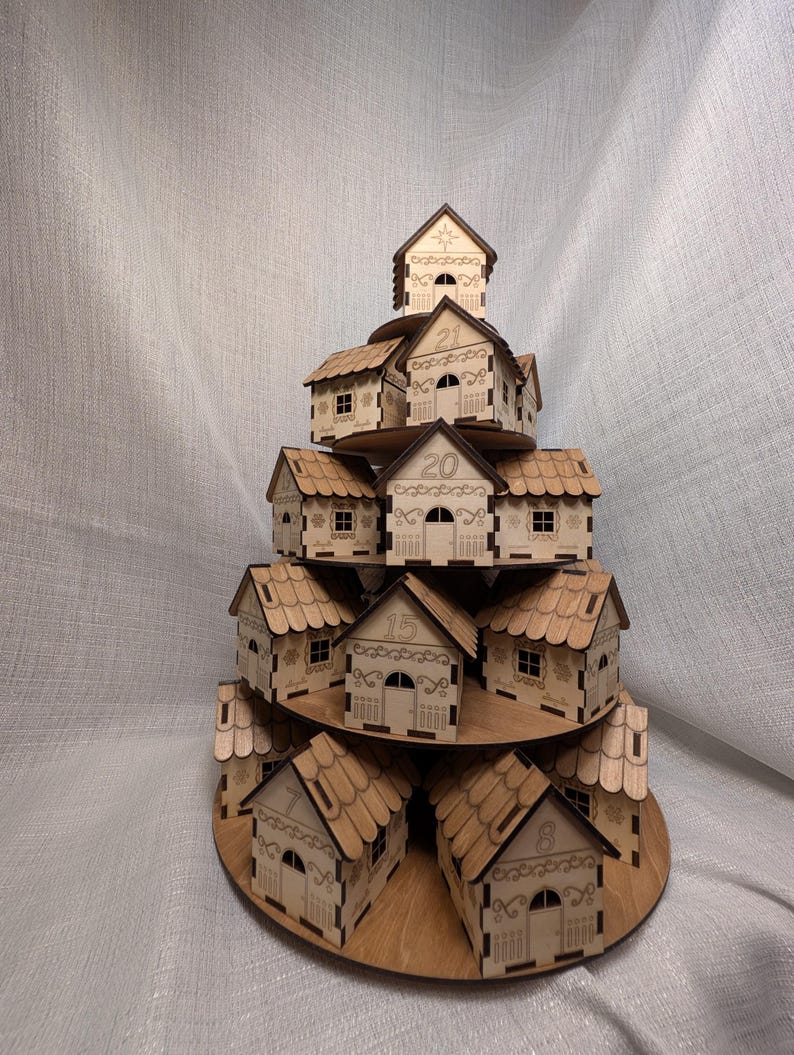 May include: A wooden advent calendar in the shape of a tiered village. Each house is laser-cut with detailed doors, windows, and patterns. Numbers are etched on the houses. The calendar is made of light brown wood.