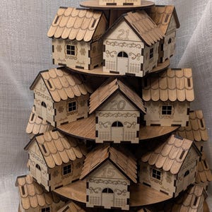 May include: A tiered wooden display of small, laser-cut houses, each with a number from 1 to 21. The houses have detailed roofs, doors, and windows. The display is made of light brown wood and resembles a Christmas tree.