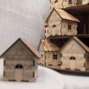 May include: A display of miniature wooden houses, each with intricate cut-out details. The houses feature pitched roofs, arched doorways, and small windows. They are arranged on tiered platforms, forming a small village. The wood has a natural, light brown colour.
