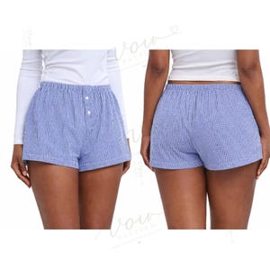 Puede incluir: Pantalones cortos tipo b&oacute;xer de cuadros vichy en azul y blanco, con cintura el&aacute;stica y una tapeta frontal con dos botones blancos. Los pantalones se muestran desde la parte delantera y trasera, exhibiendo un patr&oacute;n de cuadros cl&aacute;sico en la tela.