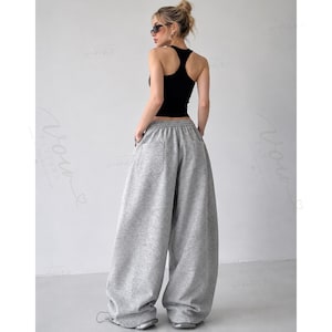 May include: A black racerback vest top paired with loose-fitting, wide-leg heather grey sweatpants. The sweatpants feature an elasticated waistband, a back pocket, and a relaxed, baggy silhouette that extends to the floor, covering the footwear.