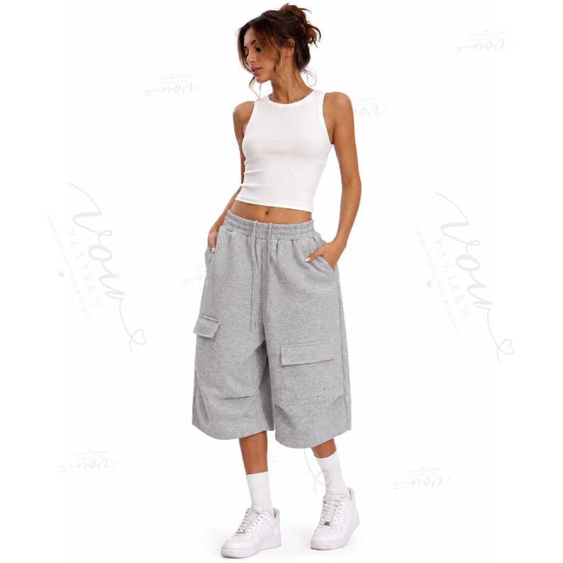 May include: A white sleeveless ribbed tank top paired with grey knee-length cargo shorts featuring side pockets and a drawstring waist. The outfit is completed with white crew socks and white athletic sneakers, creating a neutral-toned ensemble.