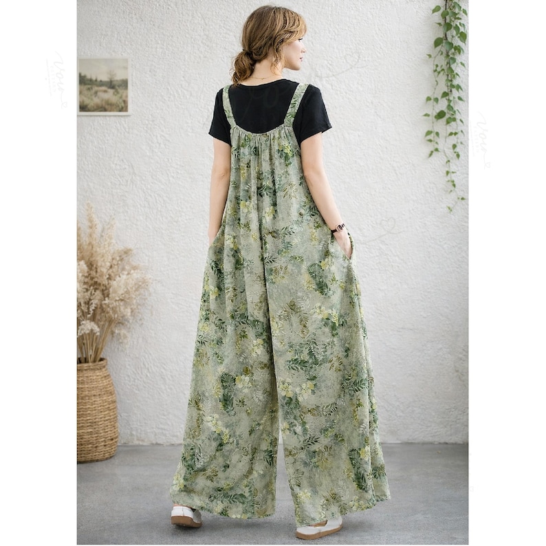 May include: A sleeveless, wide-leg jumpsuit featuring a light green base with an all-over botanical print of leaves and flowers in shades of green and yellow, worn over a plain black short-sleeved t-shirt with a round neckline.