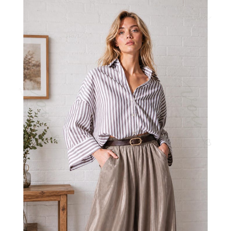 May include: A long-sleeved button-down shirt featuring vertical white and grey stripes, paired with high-waisted metallic taupe trousers. The trousers are cinched at the waist with a dark brown leather belt that has a gold-toned oval buckle.
