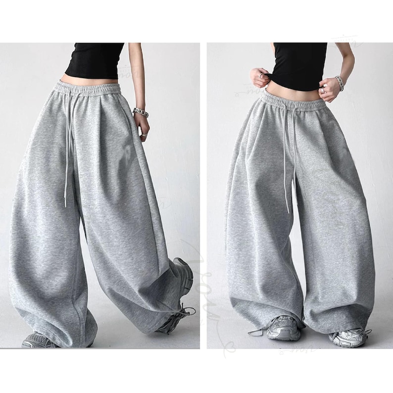May include: Light grey sweatpants featuring a high-waisted design with an elastic waistband and a drawstring closure. These wide-leg trousers have a loose, relaxed fit that drapes down to the ankles, providing a voluminous silhouette.