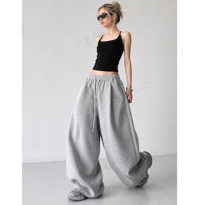 May include: A black sleeveless tank top with a square neckline paired with loose-fitting, wide-leg grey sweatpants featuring an elastic waistband and a drawstring. The sweatpants have a relaxed, baggy silhouette that extends to the floor.