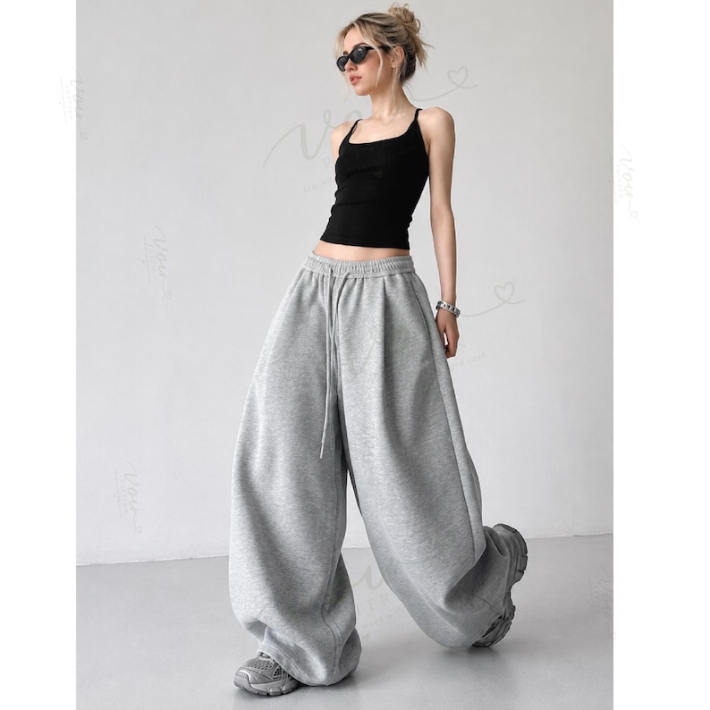 May include: A black sleeveless tank top with a square neckline paired with loose-fitting, wide-leg grey sweatpants featuring an elastic waistband and a drawstring. The sweatpants have a relaxed, baggy silhouette that extends to the floor.