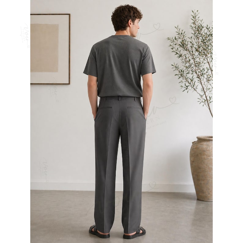 Op de afbeelding: Een antracietgrijs T-shirt met korte mouwen gecombineerd met een bijpassende antracietgrijze broek. De broek heeft een rechte snit met een strakke vouw in het midden van elke broekspijp, afgewerkt met zwarte sandalen.