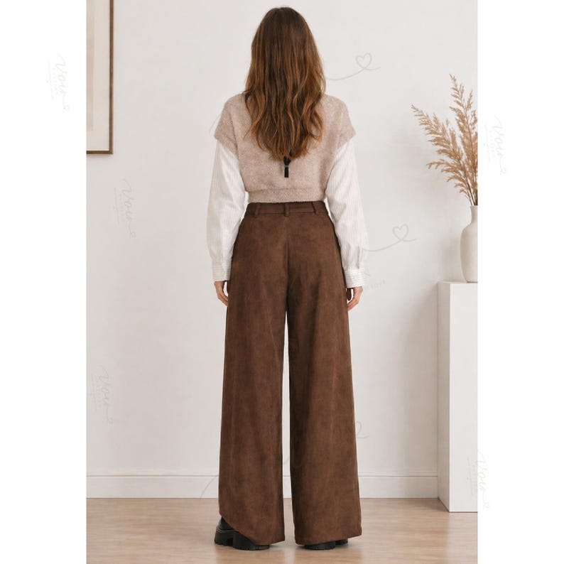 May include: A pair of dark brown wide-leg trousers paired with a white long-sleeved shirt and a beige sleeveless knit vest. The trousers feature a high-waisted design with belt loops and a smooth, matte texture, worn with black shoes.
