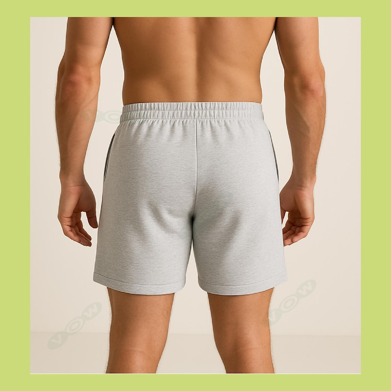 May include: Light gray athletic shorts featuring an elasticized waistband with a drawstring-free design, a smooth fabric texture, and a clean hemline. The shorts are shown from the back, displaying a simple, unadorned construction with side seams.