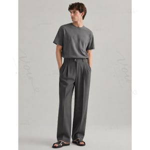 Op de afbeelding: Een antracietgrijs T-shirt met korte mouwen en ronde hals, gecombineerd met een bijpassende antracietgrijze pantalon met plooien, een enkele knoopsluiting in de taille en rechte pijpen, gedragen met zwarte open sandalen.