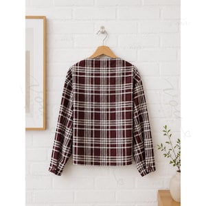 May include: A long-sleeved shirt in a deep burgundy and white plaid pattern. The shirt features a straight hemline, a simple neckline, and cuffs on the sleeves that are each secured with a single matching burgundy button, all displayed on a hanger.
