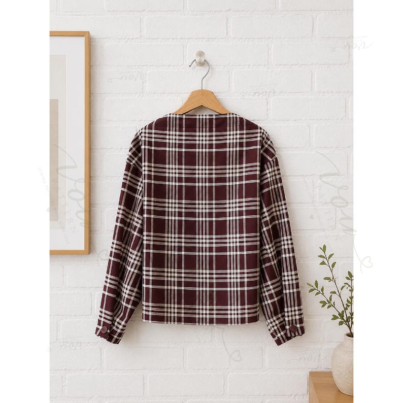 May include: A long-sleeved shirt in a deep burgundy and white plaid pattern. The shirt features a straight hemline, a simple neckline, and cuffs on the sleeves that are each secured with a single matching burgundy button, all displayed on a hanger.