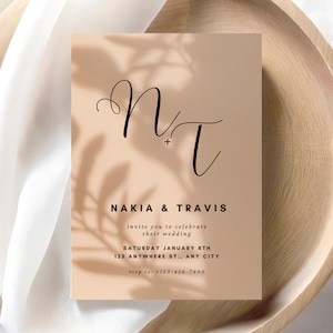 May include: A wedding invitation with a minimalist design. The card features the initials "NT" in elegant black script, along with the names "Nakia & Travis" and wedding details. The background is a soft beige with a subtle leaf shadow.