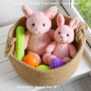May include: A woven basket filled with two pink bunny dolls, pet toys, and the text "One doll + two bags of pet snacks + six pet toys." The basket also contains a green cucumber-shaped toy, an orange ball, and a purple ball.