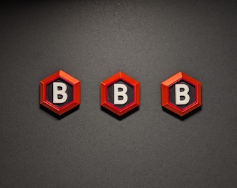 May include: Three red and black hexagon-shaped objects with a white letter "B" in the center. The objects are arranged in a horizontal line against a dark gray background. The objects have a glossy finish.