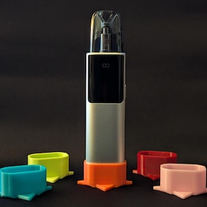 May include: A silver electronic device with a black display and a clear top cap, standing upright in an orange base. Four additional oval-shaped bases in blue, lime green, red, and light pink are arranged around the central device.