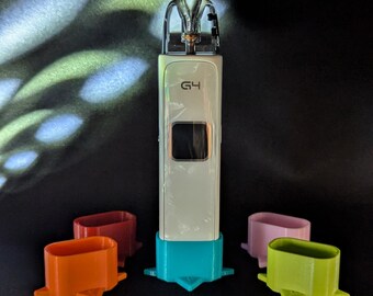 May include: A white and teal vape device with the text "G4" is displayed. Four colored mouthpieces in orange, red, pink, and green are arranged around the device. The background is black with a pattern of light.