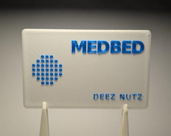 May include: A white rectangular sign with the blue text "MEDBED" at the top and "DEEZ NUTZ" at the bottom. A blue dot pattern is on the left side of the sign. The sign is supported by two white stands.