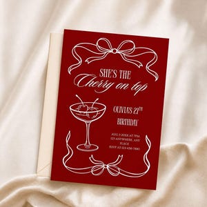 Op de afbeelding: Een rode verjaardagskaart met witte tekst en illustraties. De tekst luidt "She's the Cherry on top" en bevat de naam "Olivia" en de leeftijd "27th". Een cocktailglas met kersen is ook afgebeeld.