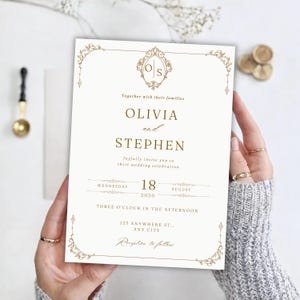 Op de afbeelding: Een witte trouwkaart met gouden tekst en sierlijke gouden filigraanranden. De tekst luidt Olivia and Stephen, together with their families, joyfully invite you to their wedding celebration op woensdag 18 augustus 2030.